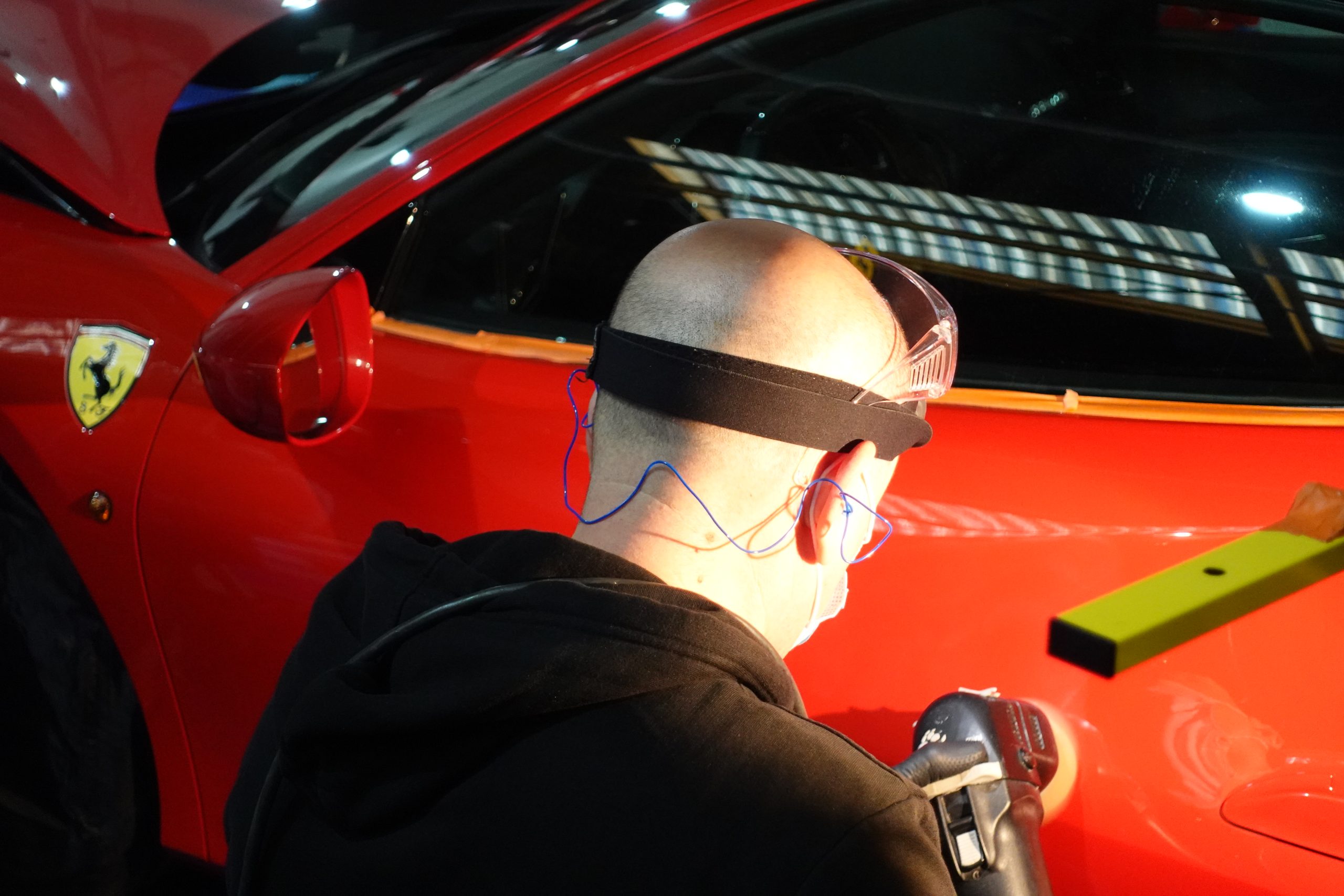 Detailer polissant l’aile d’une Ferrari rouge sous une rampe d’éclairage, formation devenir detailer en Suisse