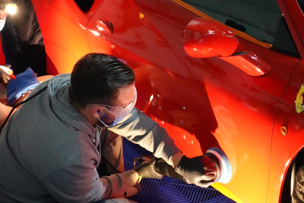 Stagiaire polissant la carrosserie d’une voiture de sport rouge à la polisseuse, formation detailing en Suisse